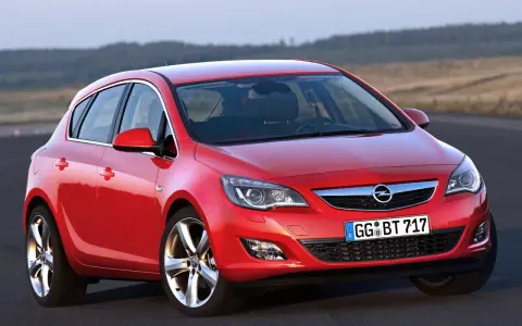Czerwony Opel Astra 4 na drodze, z widokiem na wzgórza w tle.