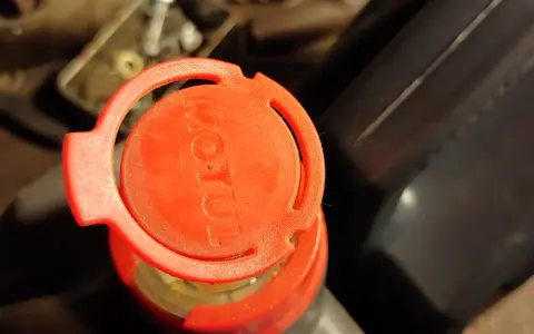 Czerwona nakrętka z logo Motul na opakowaniu oleju silnikowego.
