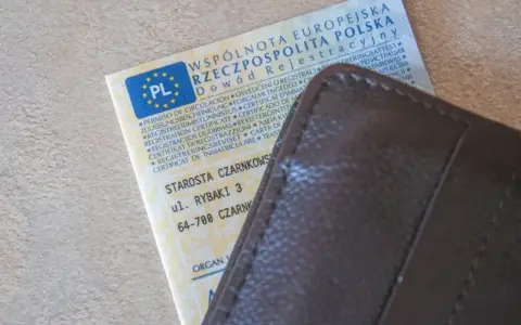 Dowód rejestracyjny pojazdu z PL i adresem Starostwa Czarnkowskiego, schowany w brązowym etui. Po rejestracja dokument gotowy do drogi.