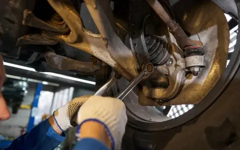 Mechanik dokręca śrubę w zawieszeniu samochodu kluczem.
