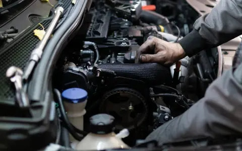 Mechanik pracuje przy silniku benzynowym, jego ręce są ubrudzone smarem.