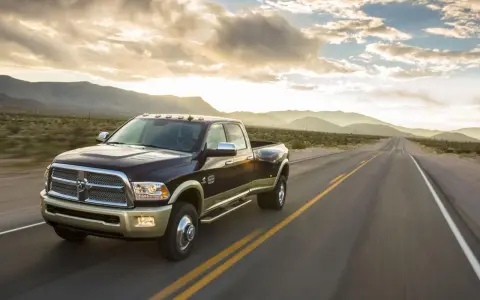 Ciemnobrązowy Dodge Ram 2500 z dwoma rzędami kół jedzie pustynną drogą o zachodzie słońca.