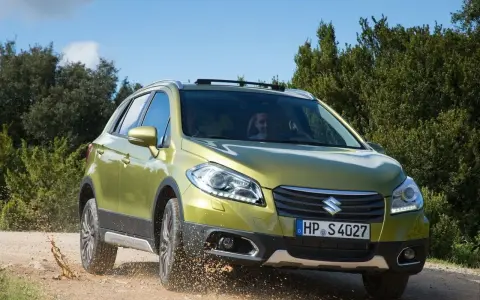 Zielony Suzuki SX4 S-Cross pokonuje teren, wzbijając kurz. Mimo że auto radzi sobie na bezdrożach, warto rozważyć jego wady przed zakupem.