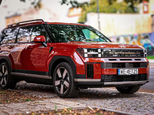 Czerwony Hyundai Santa Fe z nowoczesnym designem stoi na brukowanej drodze, otoczony jesiennymi liśćmi.