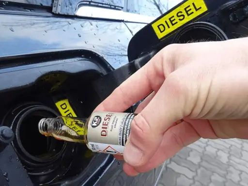 Ręka wlewa dodatek do diesla z małej buteleczki do baku samochodu.