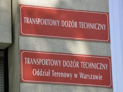 Dwa czerwone szyldy z białym napisem "TRANSPORTOWY DOZÓR TECHNICZNY". Dolny szyld zawiera dodatkowo "Oddział Terenowy w Warszawie". Miejsce, gdzie można uzyskać homologację.