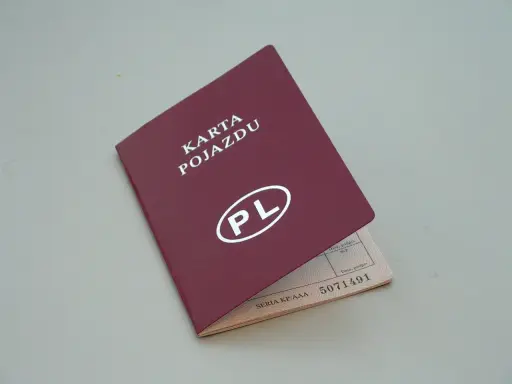 Czerwona karta pojazdu z białym napisem "PL" i numerem seryjnym. Dokument jest otwarty, ukazując dane pojazdu.