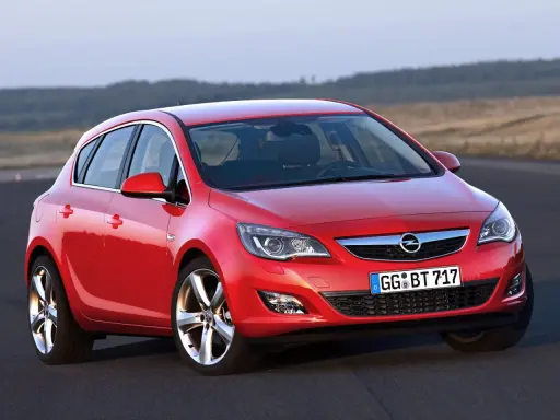 Czerwony Opel Astra 4 na drodze, z widokiem na wzgórza w tle.