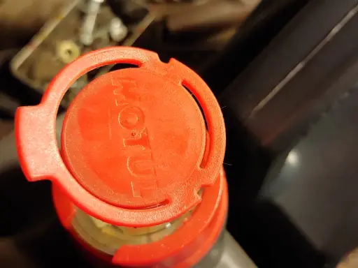 Czerwona nakrętka z logo Motul na opakowaniu oleju silnikowego.
