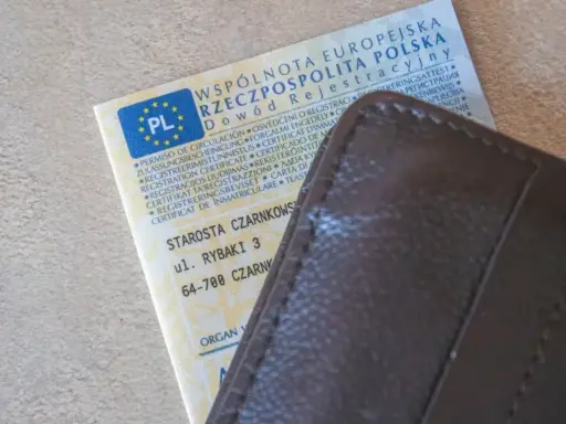 Dowód rejestracyjny pojazdu z PL i adresem Starostwa Czarnkowskiego, schowany w brązowym etui. Po rejestracja dokument gotowy do drogi.
