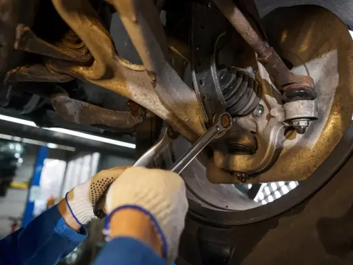 Mechanik dokręca śrubę w zawieszeniu samochodu kluczem.