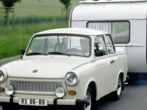 Biały Trabant ciągnie przyczepę kempingową po drodze.