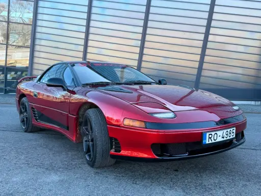 Czerwony Mitsubishi 3000GT z czarnymi felgami i przyciemnianymi szybami, zaparkowany przed nowoczesnym budynkiem.