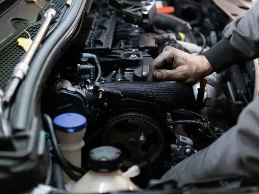 Mechanik pracuje przy silniku benzynowym, jego ręce są ubrudzone smarem.