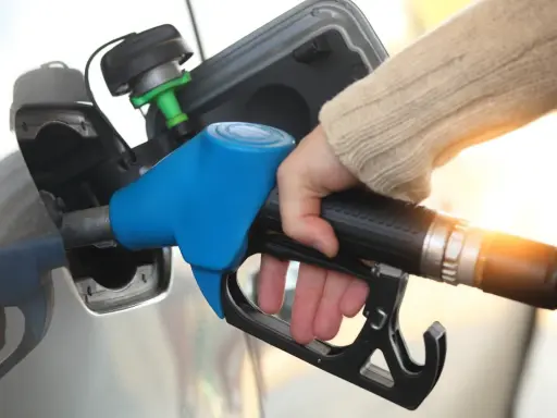 Dłoń trzymająca niebieski pistolet do tankowania paliwa przy samochodzie.