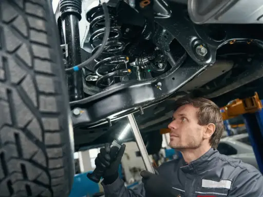Mechanik bada podwozie samochodu, oświetlając latarką skomplikowany wielowahacz i sprężynę amortyzatora.