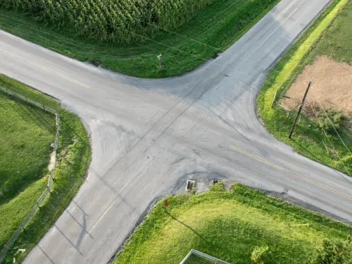 Rozjazd dróg na wsi, gdzie obowiązuje zasada prawej ręki. Wokół pola kukurydzy i zielone łąki.