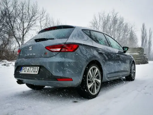Szary Seat Leon FR w zimowej scenerii, pokryty śniegiem.