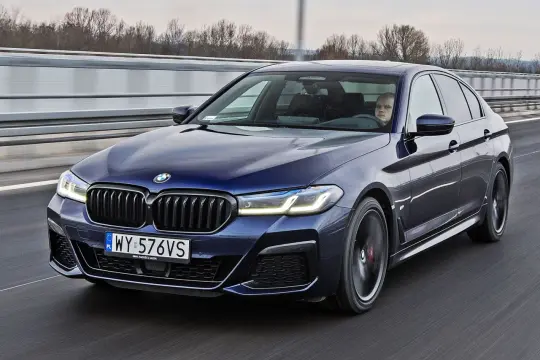 Ciemnoniebieskie BMW 520d xDrive jedzie autostradą. Kierowca zamyślony.