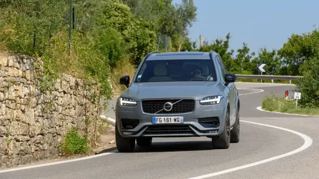 Szary Volvo XC90 2020 pokonuje zakręt na malowniczej, górskiej drodze.