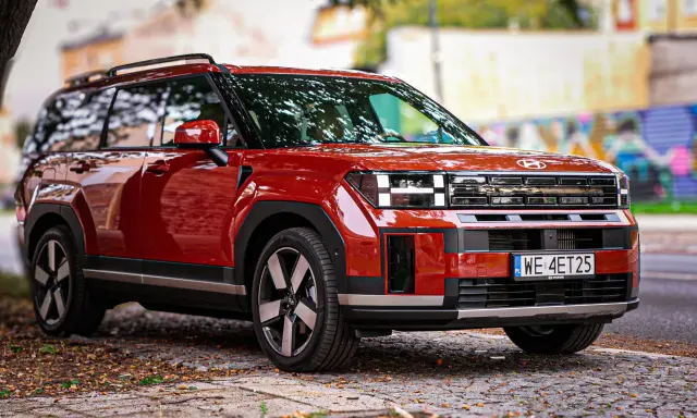 Czerwony Hyundai Santa Fe z nowoczesnym designem stoi na brukowanej drodze, otoczony jesiennymi liśćmi.