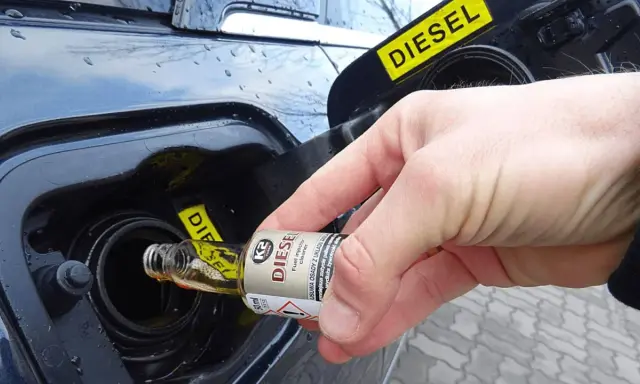 Ręka wlewa dodatek do diesla z małej buteleczki do baku samochodu.