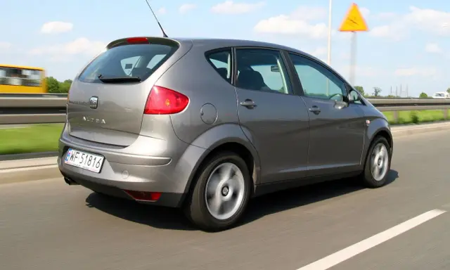 Szary Seat Altea XL jedzie autostradą. W tle widać żółty autobus i znak ostrzegawczy.