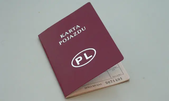 Czerwona karta pojazdu z białym napisem "PL" i numerem seryjnym. Dokument jest otwarty, ukazując dane pojazdu.
