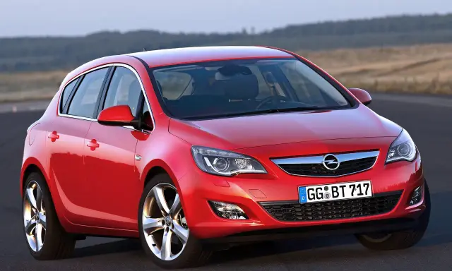 Czerwony Opel Astra 4 na drodze, z widokiem na wzgórza w tle.