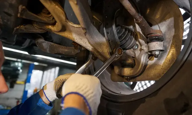 Mechanik dokręca śrubę w zawieszeniu samochodu kluczem.