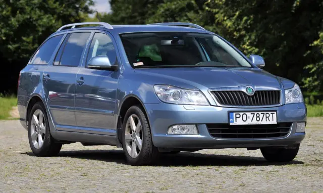 Niebieska Skoda Octavia 2010 kombi stoi na brukowanym podjeździe, otoczona zielenią.