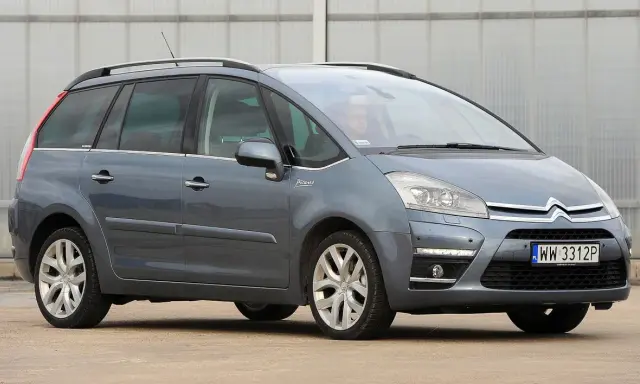 Szary Citroen Picasso z napisem "Picasso" na błotniku, zaparkowany przed budynkiem.