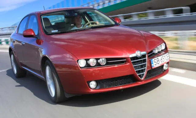 Czerwone Alfa Romeo 159 1.9 JTD pędzi po autostradzie.