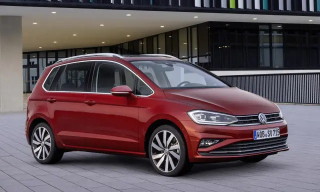 Czerwony Volkswagen Golf Sportsvan przed nowoczesnym budynkiem. Wady tego modelu mogą dotyczyć np. wyciszenia kabiny.