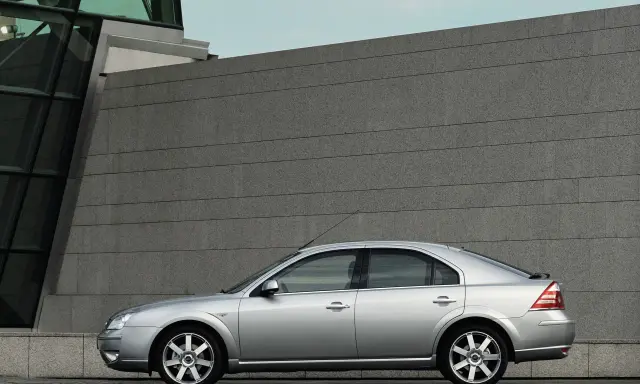 Srebrny Ford Mondeo MK3 2.0 TDCI stoi przed nowoczesnym budynkiem z kamienną fasadą.