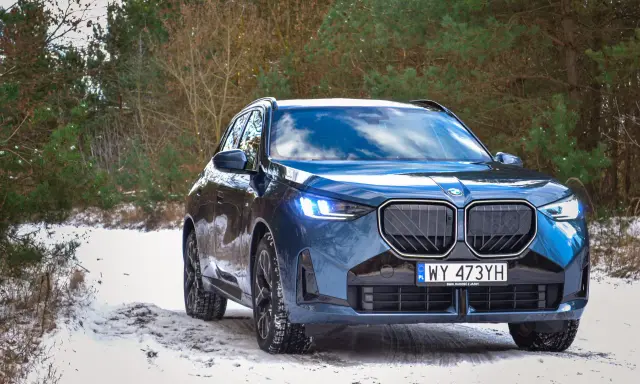 Niebieskie, nowe BMW X3 na ośnieżonej drodze w lesie. Zimowe opony gotowe na wyzwania.