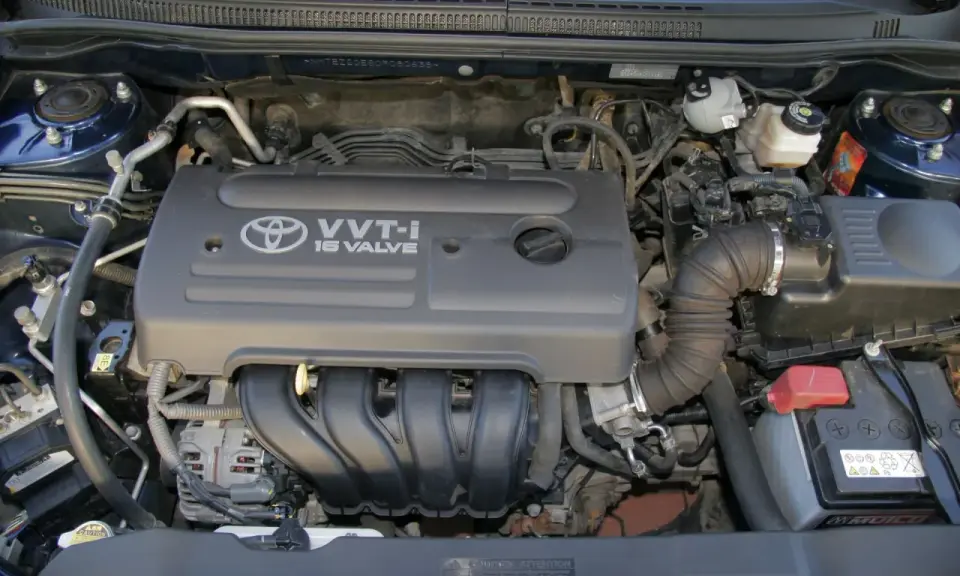 Silnik VVT-i 16 Valve z Toyoty Corolla E12. Widoczny alternator, akumulator i elementy układu dolotowego.