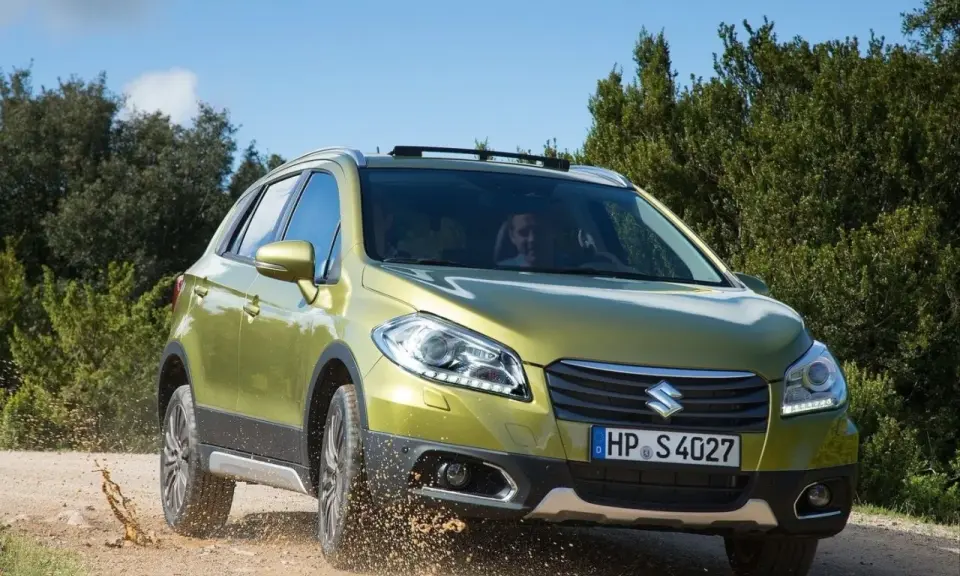 Zielony Suzuki SX4 S-Cross pokonuje teren, wzbijając kurz. Mimo że auto radzi sobie na bezdrożach, warto rozważyć jego wady przed zakupem.
