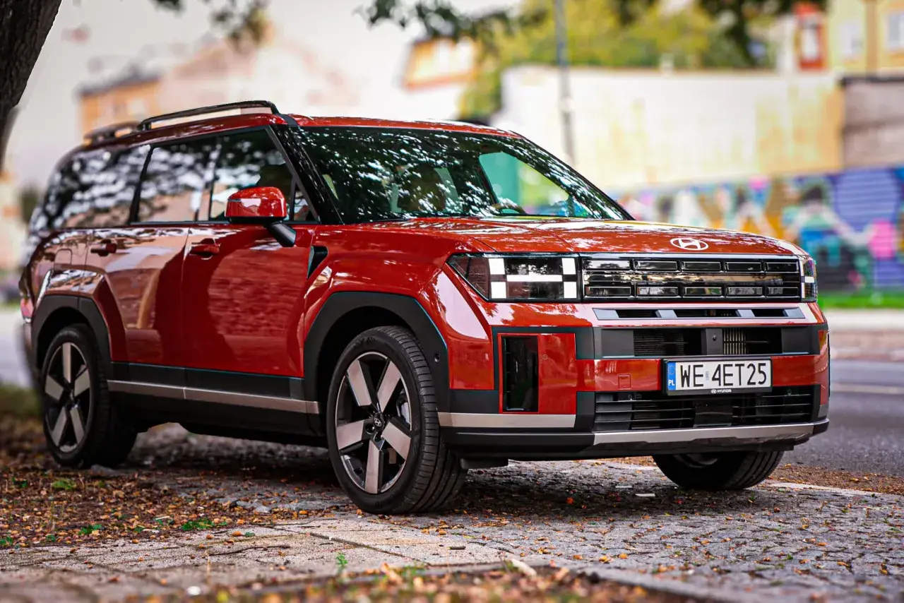 Czerwony Hyundai Santa Fe z nowoczesnym designem stoi na brukowanej drodze, otoczony jesiennymi liśćmi.