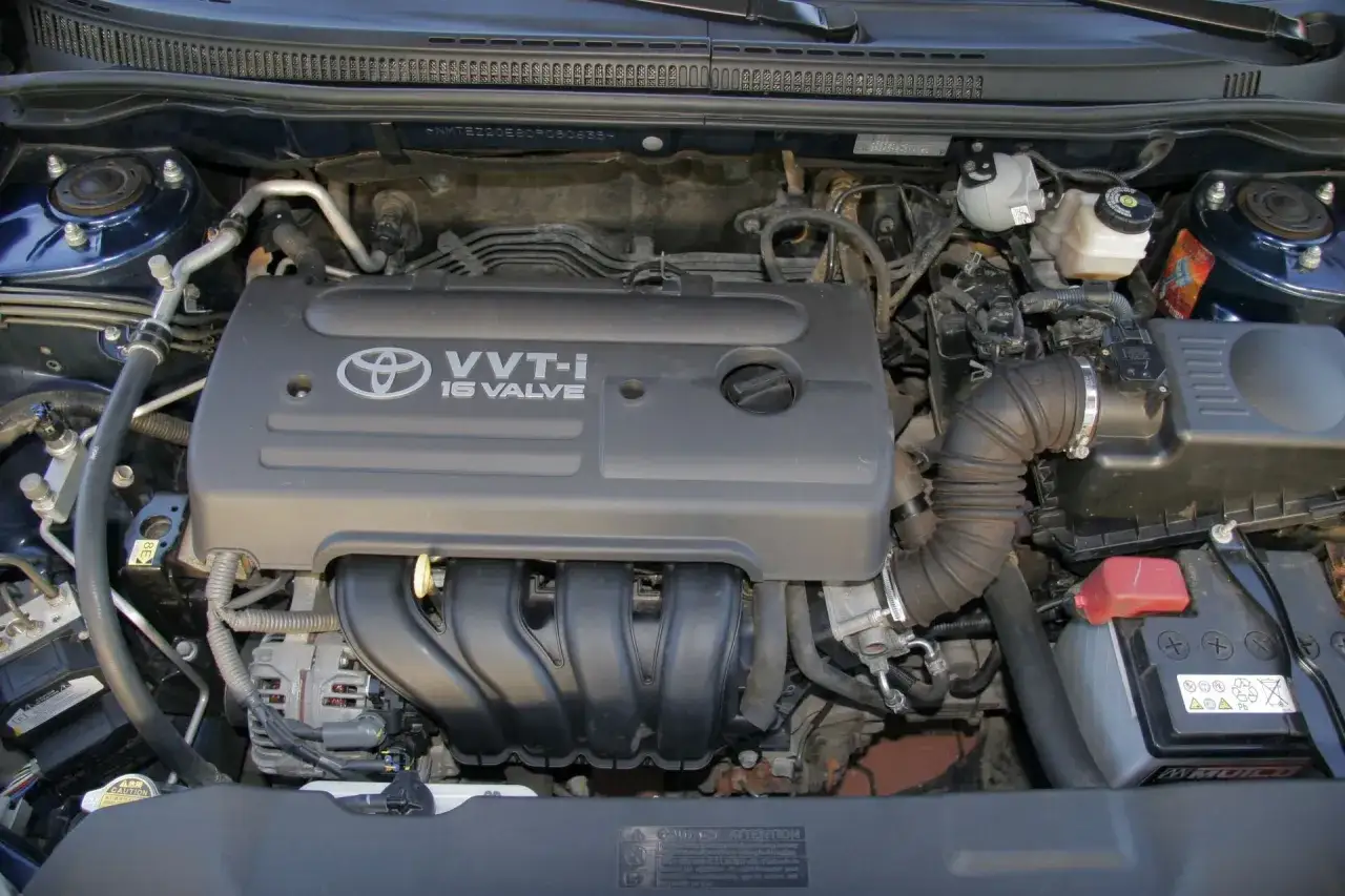 Silnik VVT-i 16 Valve z Toyoty Corolli 2004. Widoczny alternator, akumulator i elementy układu dolotowego.