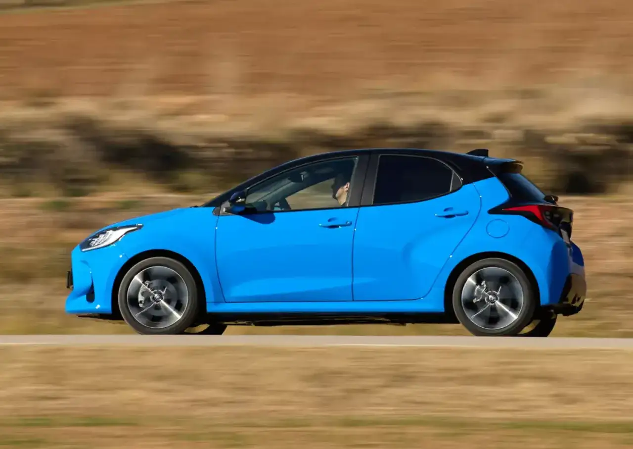 Niebieski hatchback z czarnym dachem, idealne auto dla kobiety, pędzi po drodze.