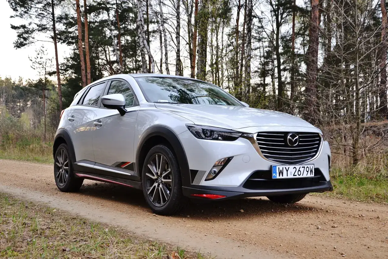 Srebrna Mazda CX-3 na leśnej drodze. Elegancki SUV z charakterystycznymi detalami, gotowy na przygodę wśród drzew.