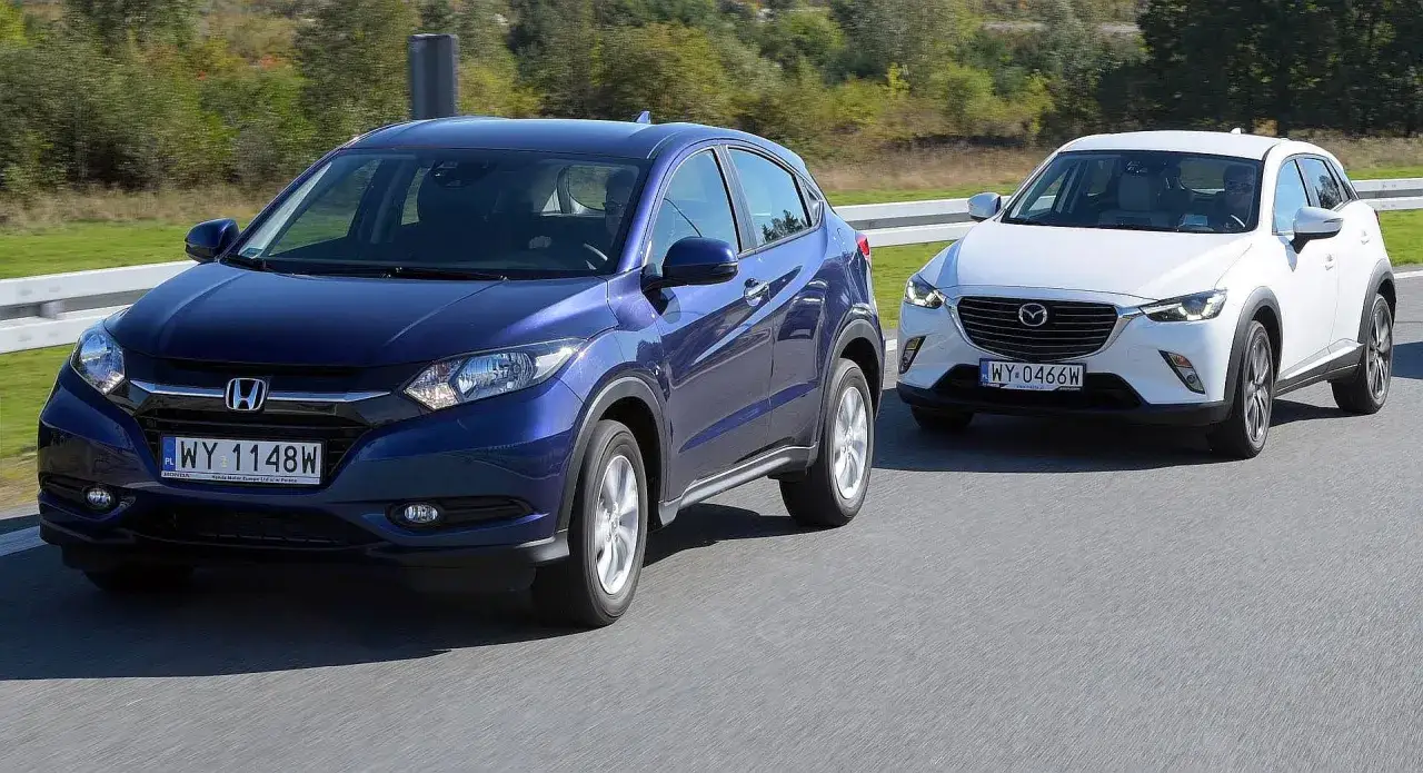 Niebieski Honda HR-V i biała Mazda CX-3, przykłady najmniej awaryjnych SUV-ów 10 letnich, jadące po drodze.