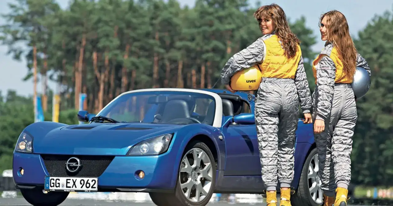 Dwie kobiety w kombinezonach wyścigowych stoją obok niebieskiego Opla Speedstera.