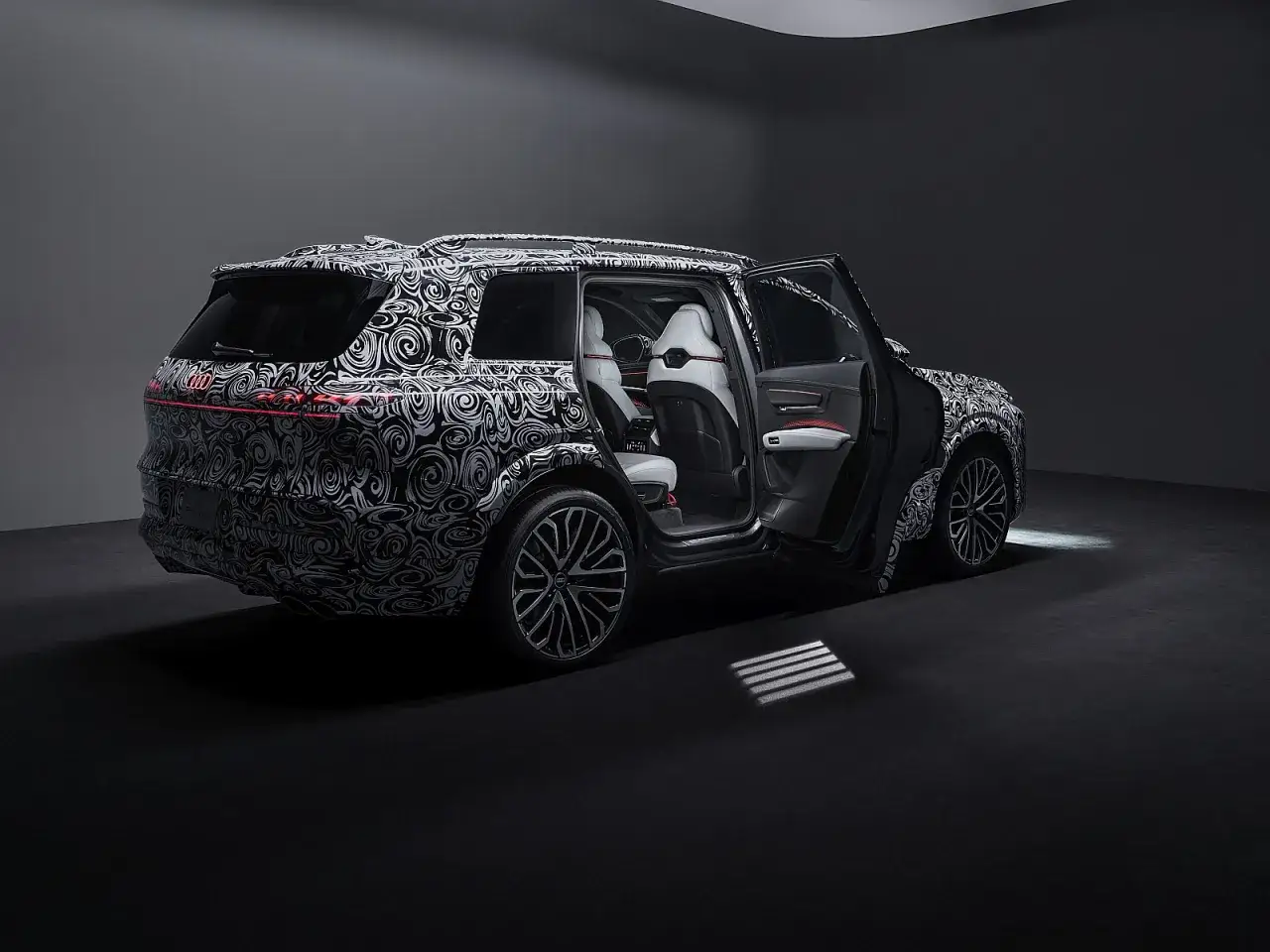 Nowy Audi V8 w kamuflażu, z otwartymi drzwiami, prezentuje eleganckie wnętrze i sportowe felgi.