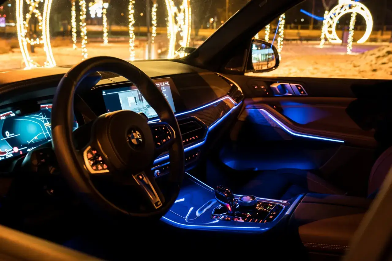 Wnętrze BMW X5 2025 z niebieskim ambientowym oświetleniem, nocą, w tle świąteczne iluminacje.