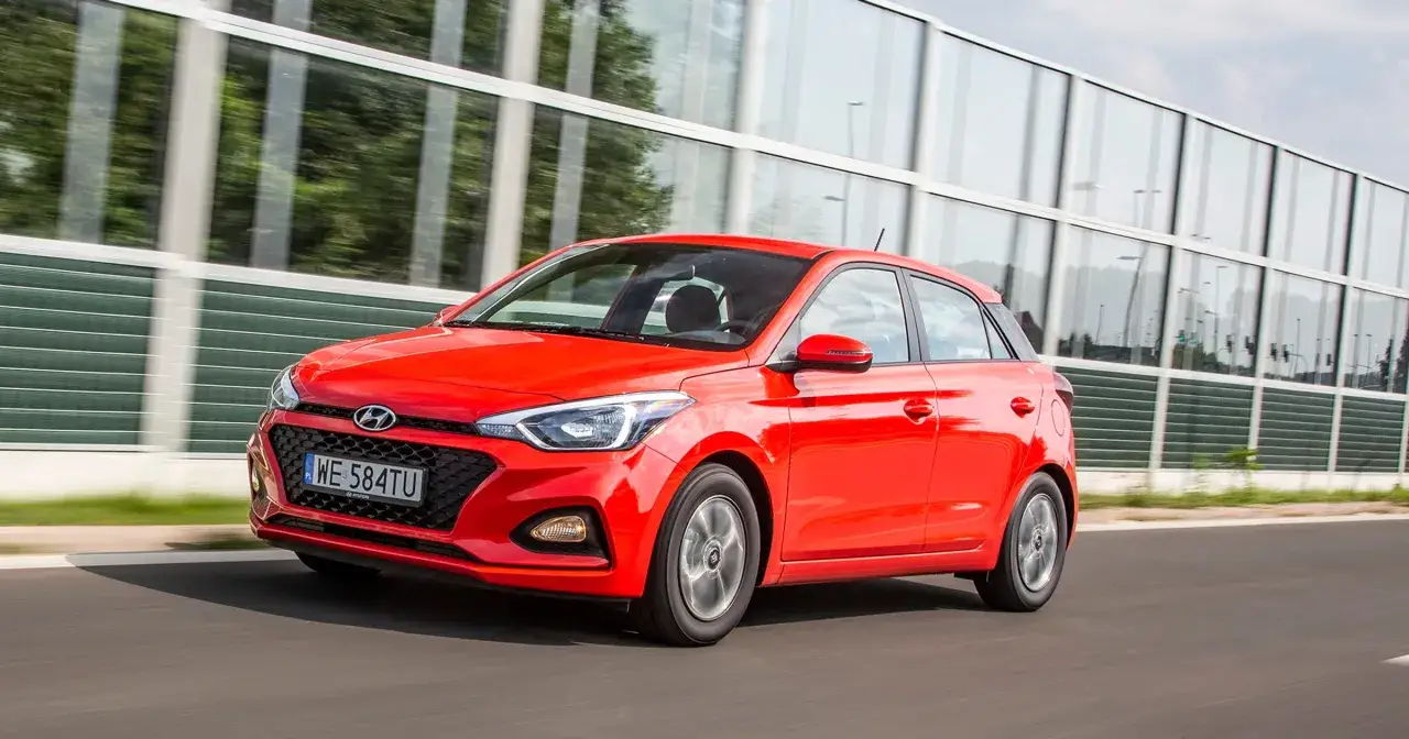 Czerwony Hyundai i20 1.2 benzyna w ruchu, z refleksami drzew w szklanej barierze dźwiękochłonnej.