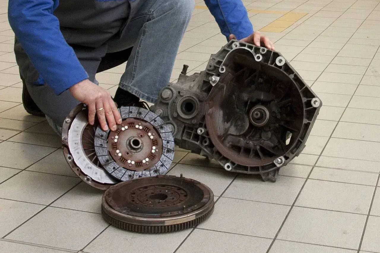 Mechanik pokazuje rozłożony zestaw sprzęgła i skrzynię biegów, co może wskazywać na uszkodzony wysprzęglik objawy.