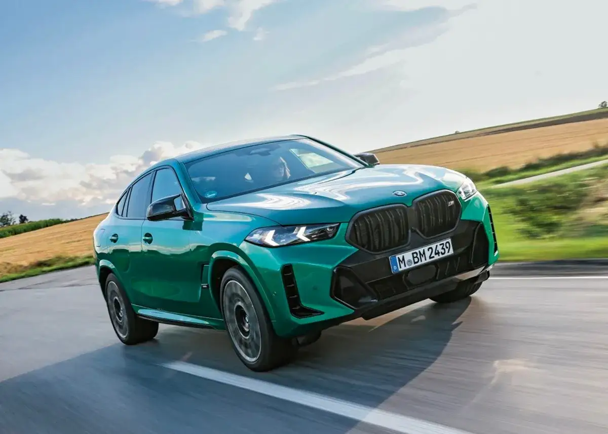 Zielony BMW X6 M Competition, jakby wyłaniał się z krajobrazu, pędzi po drodze. Ten sportowy SUV, niczym drapieżnik, gotów jest na każde wyzwanie.