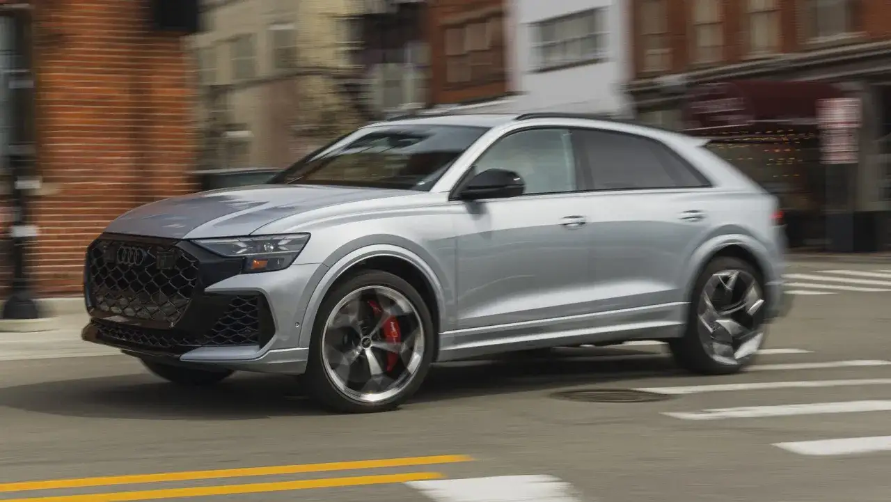Srebrny Audi RSQ8 pędzi ulicą, zamazane budynki w tle.